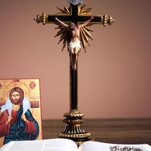 Decorative crucifix with Jesus Christ on a brown background, next to an open book and a religious icon.