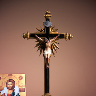Decorative crucifix with Jesus Christ on a brown background, next to an open book and a religious icon.