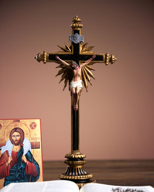 Decorative crucifix with Jesus Christ on a brown background, next to an open book and a religious icon.
