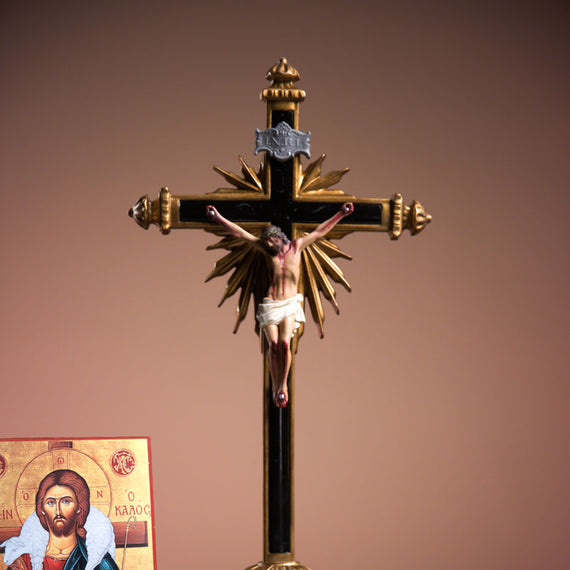 Decorative crucifix with Jesus Christ on a brown background, next to an open book and a religious icon.